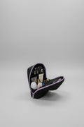 A black makeup bag with purple trim, shown open on a white table with various cosmetics inside. The background is a blurred indoor room.
